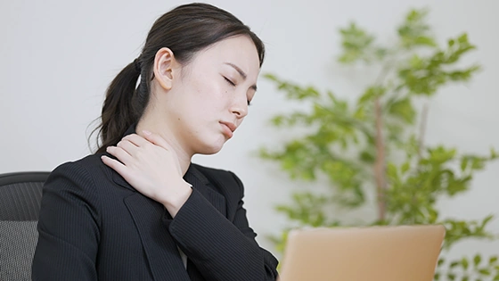 首の痛みで仕事を中断する女性
